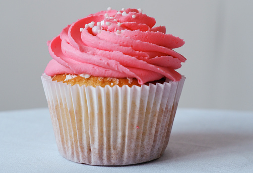 Cupcake with raspberries and pink whipped cream, decorated with edible beads. Festive cupcake. Close-up. Birthday concept