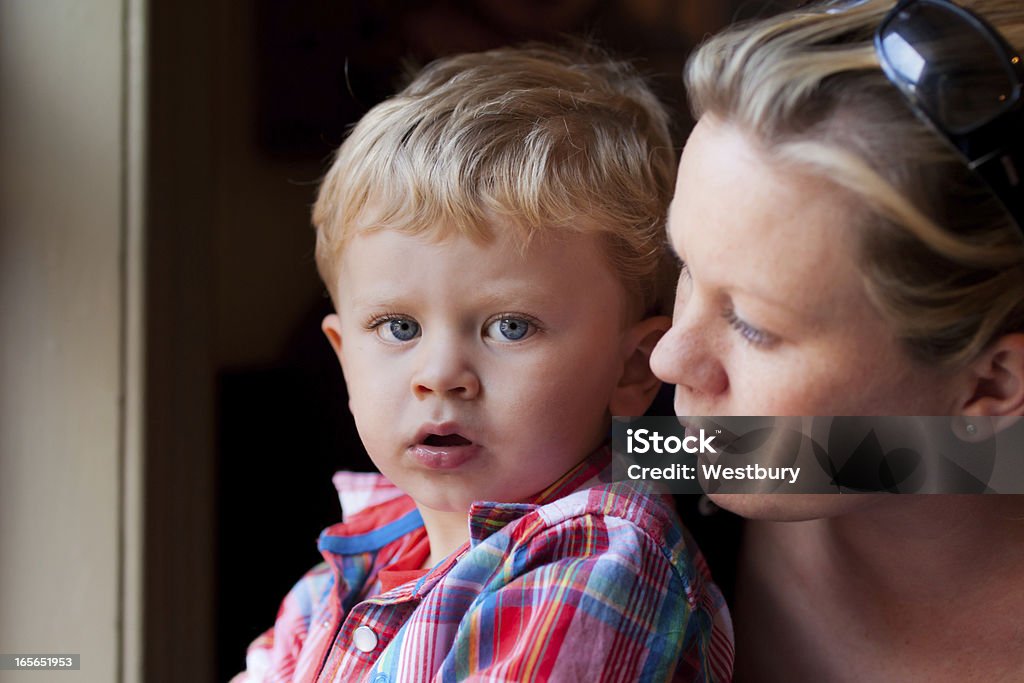 Blond mother and son sitting at window A boy makes eye contact as his mother looks out a window over his shoulder. Child Stock Photo