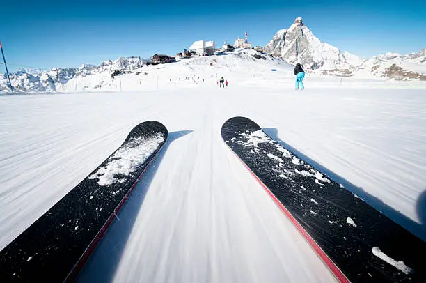 Low angle view with the camera at ankle level as the skiier in a schuss position speeds along a piste in the European Alps.