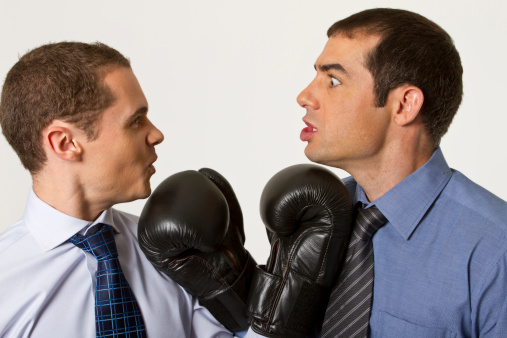 Two young  business managers confront themselves with boxing gloves; business disagreement or competition concept (studio shot).