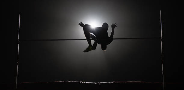 Male high jumper jumping over the bar against black background.