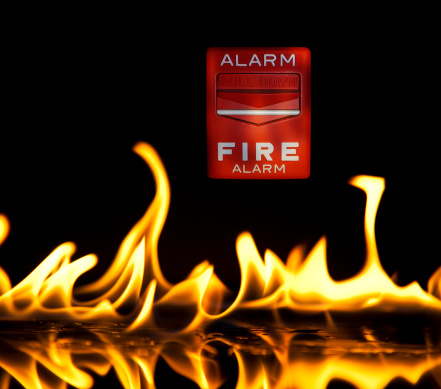 Fire alarm in fire flames on black background.