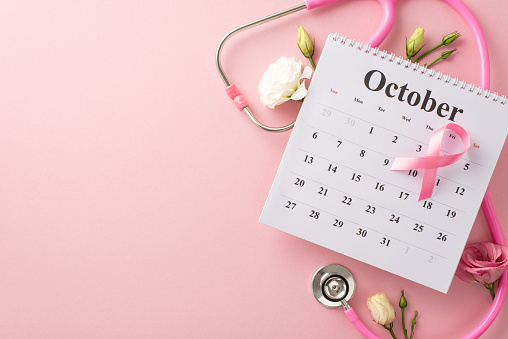 Health calendar setup. Top view shot of October month, stethoscope, pink ribbon, and natural eustoma flowers on pastel pink backdrop, making it ideal for awareness campaigns or promotions