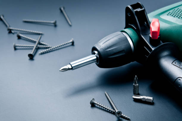 Composition of electric drill with screws and screwdrivers on dark background.
