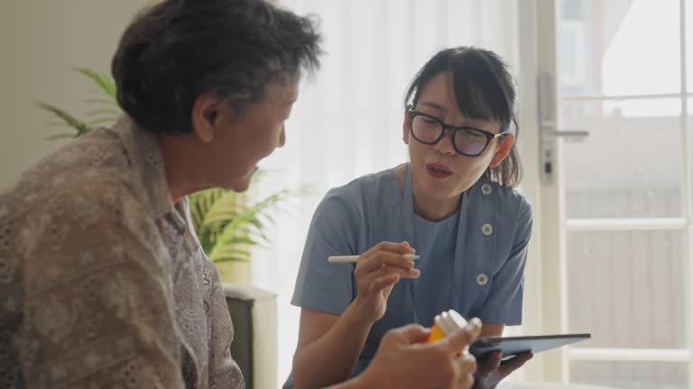 A female caregiver looks after the medication of an elderly woman at home.