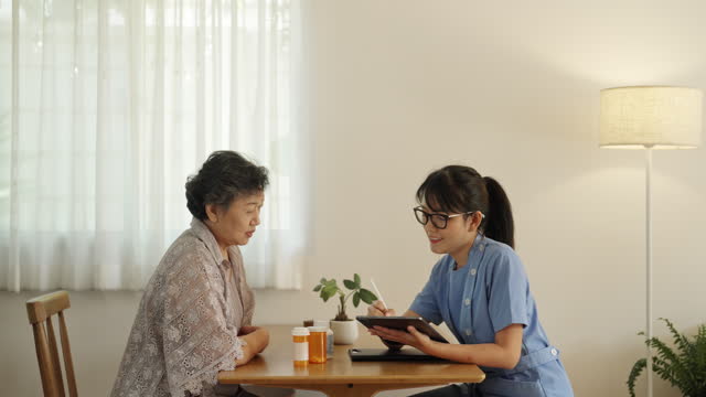 A female caregiver looks after the medication of an elderly woman at home.
