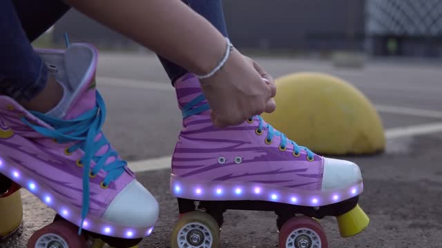Young girl tying shoelaces on vintage roller skates with LED lights on her leg.