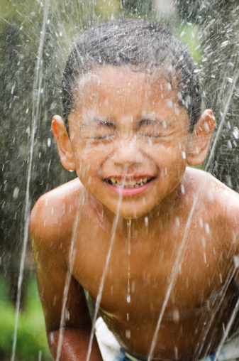 Little hispanic boy playing in a water sprinkler to cool down in the hot summer.