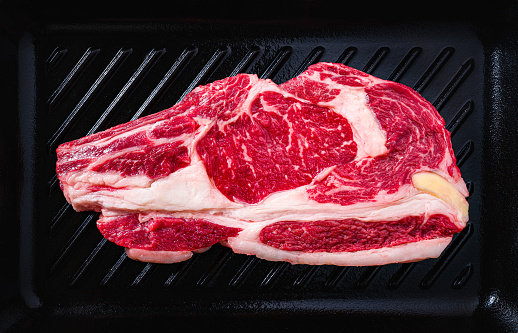 Beef rib steak raw vivid on a cast iron grill black background uncooked  top view flatlay