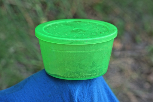 one closed round green plastic worm box standing on a blue table outdoors on a gray background