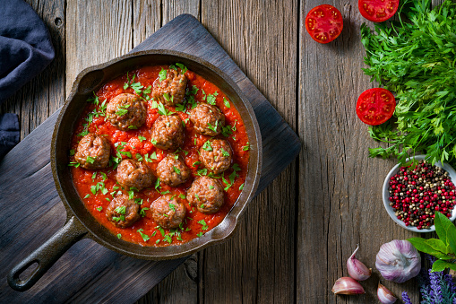 Meat balls with tomato sauce homemade in rustic cast iron pan over wooden table board with ingredients
