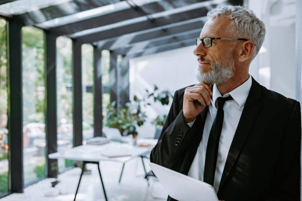 istock Confident mature businessman holding digital tablet and looking away while standing in office 1656801786