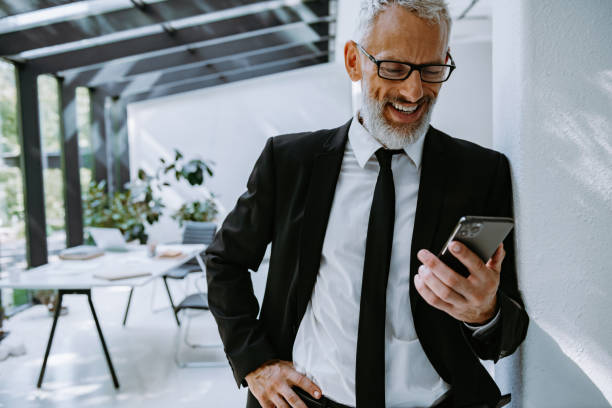 istock Happy mature businessman looking at smart phone while standing in the modern office 1656802302