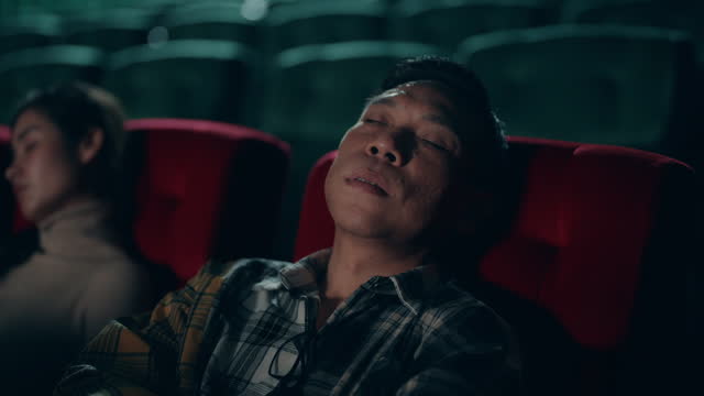 Asian Man Finding Serenity: Falling Asleep in a Cozy Movie Theater.