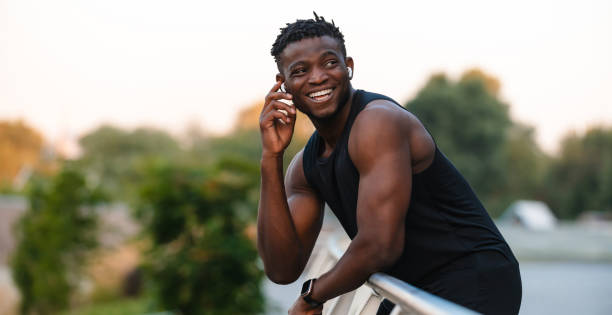 Happy African man in sportswear adjusting his headphones while relaxing after training outdoors