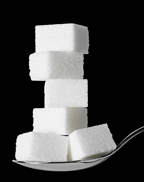 Sweet Tooth: Too Much Sugar Sugar cubes stacked up on a teaspoon.  Black background. sugar cube stock pictures, royalty-free photos & images