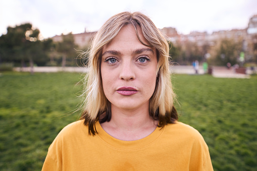 Portrait of a woman looking at camera outdoors with serious expression. Beautiful girl is cute. She looks unsmiling and attractive and confident. This caucasian female is posing sadness