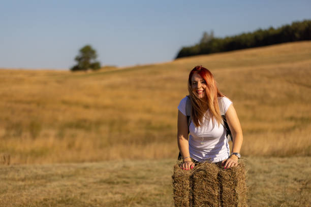 A young woman with blond hair lies on a haystack in summer, top view