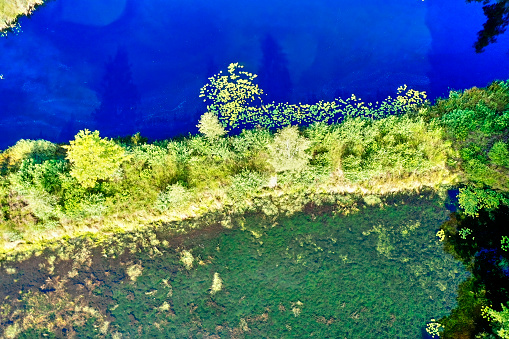 Abstract looking aerial view of overgrown land strip between deep blue pond and clear pond with water plants