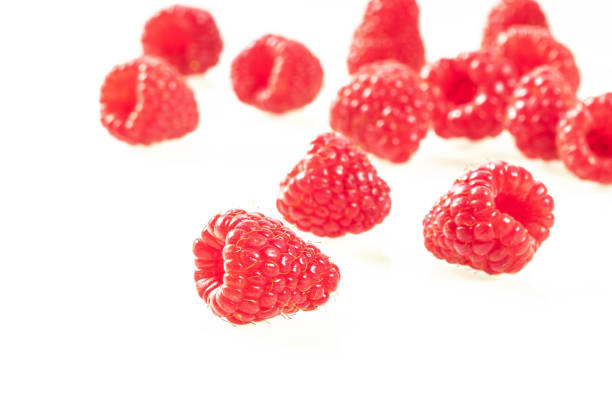 A macro perspective of a pile of ripe, red raspberries against a bright, white background. The berries' detailed texture and vivid color evoke freshness and a healthy lifestyle, making it ideal for culinary and wellness concepts. The composition emphasizes their natural vibrancy and nutritional appeal.