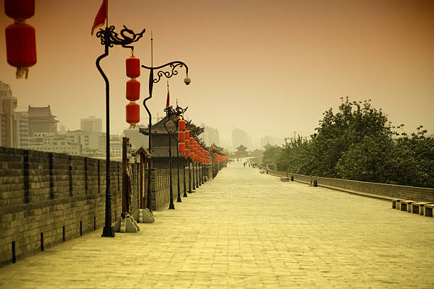 Fortress gate tower with ornate Chinese roofline, double-tiered turquoise structure, watchtower fortification, moat waterway, landscape perspective, heritage