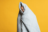 Girl wrapped in warm duvet. Woman covering in cosy comfy blanket. Isolated on yellow.