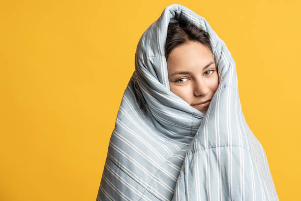 istock Sleepy girl wrapped in blanket smiling. Copy space. Isolated yellow studio background. 1657054664