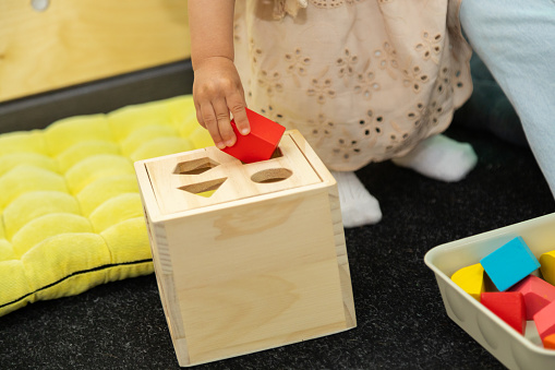 Closeup of toddler hand playing with montessori Imbucare shapes box learning early geometry and practicing fine motor skills