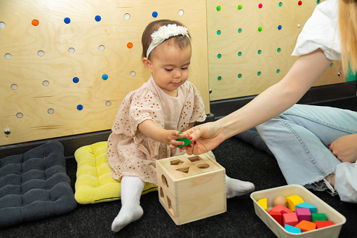Toddler girl playing with montessori Imbucare shapes box learning early geometry and practicing fine motor skills