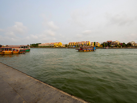 The yellow building and antique \npassenger boat on Thu Bon River, Hoi An, Vietnam.