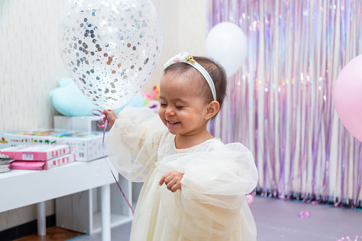 Happy baby girl in the beautiful dress playing with balloons during her birthday