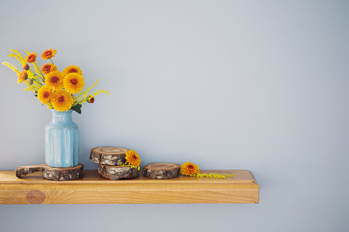 orange chrysanthemums in blue vase on wooden shelf on background wall