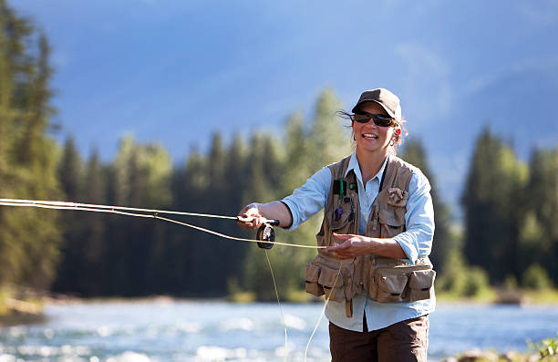 Smiling woman fly-fishing trout on a British Columbia river Woman fly Fishing in British Columbia. fly fishing stock pictures, royalty-free photos & images