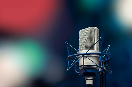 Selective focus of mouth of young smiling women recording podcast and doing live streaming using microphone and headphones in recording studio