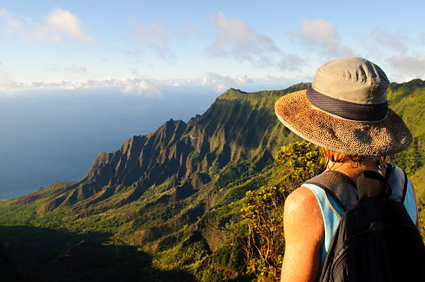 Woman outdoors looking at dramatic view and future on Kauai A woman in her fifties looking at the dramatic landscape at Kalalau Lookout on Kauai kauai photos stock pictures, royalty-free photos & images
