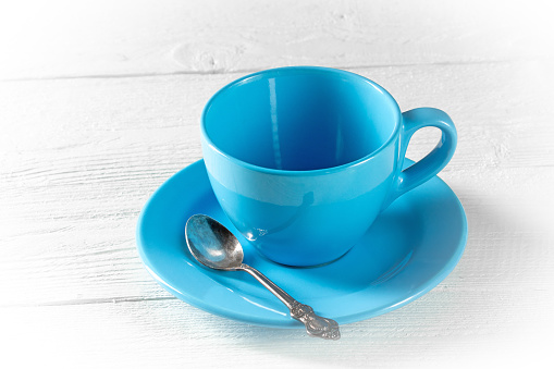 Symbol of morning coffee - an empty blue cup with a saucer for coffee on a white wooden table.