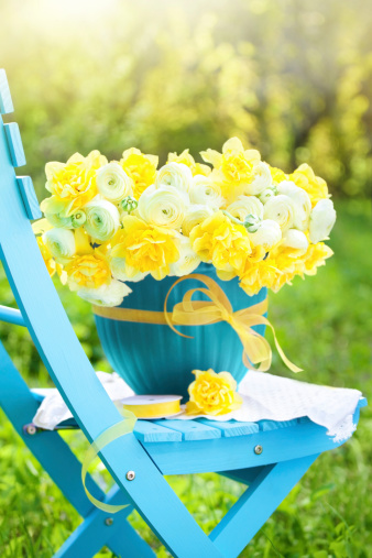 Yellow sunflowers, book and straw hat are on wooden white chair. Summer still life in garden.