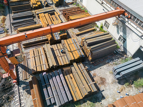 Aerial view of worker transporting stack of metal pipes with gantry crane in the steel factory