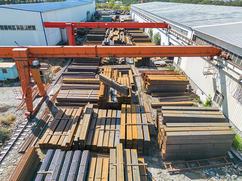 Aerial view of worker transporting stack of metal pipes with gantry crane in the steel factory