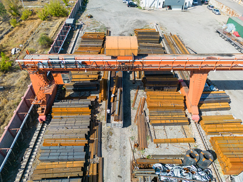 Aerial view of workers loading stack of metal pipes with gantry crane