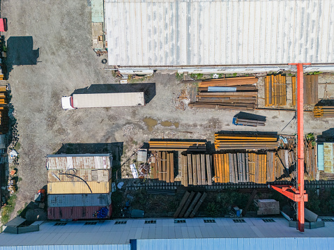 Aerial top down view of truck preparing for loading stack of metal pipes with gantry crane