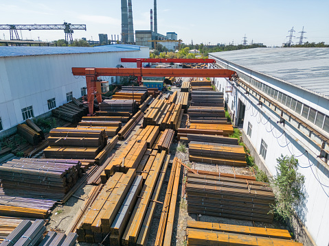 Aerial view of galvanized iron pipes stack and stainless steel rectangular bars of metal and gantry crane in the iron factory