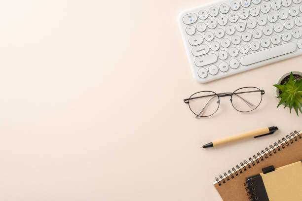 Workspace arrangement idea. Top view of keyboard, planner, notepad, pen, flowerpot, glasses on a light, neutral surface. Space for text or advertising