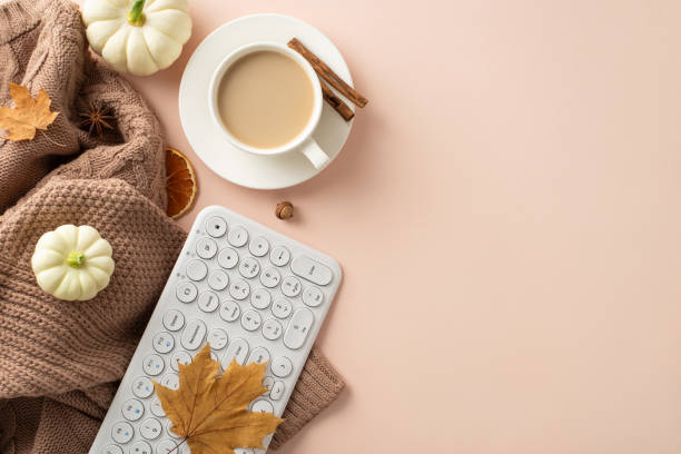 istock Cozy fall workplace concept. Top view with keyboard, comfy brown knitted sweater, fresh coffee, saucer, pattypans, acorn, cinnamon, maple leaves on soft beige background. Empty space for text or ads 1657232836