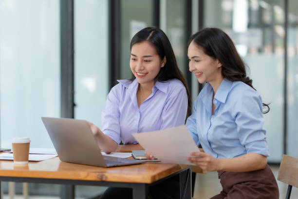 istock Two cheerful Asian office workers women collaborating on a project sitting at desk with laptop computer. 1657250305