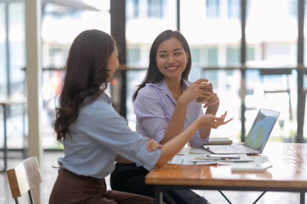 istock Two cheerful Asian office workers women collaborating on a project sitting at desk with laptop computer. 1657250839