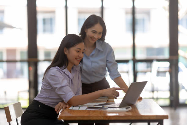 istock Two cheerful Asian office workers women collaborating on a project sitting at desk with laptop computer. 1657250862