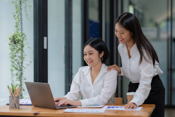 istock Two cheerful Asian office workers women collaborating on a project sitting at desk with laptop computer. 1657251373