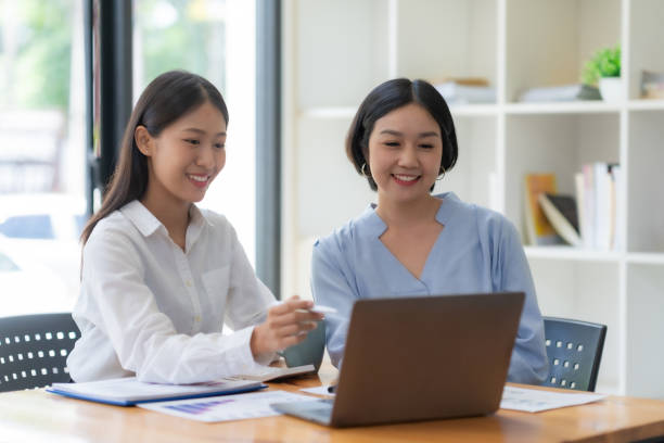 istock Two cheerful Asian office workers women collaborating on a project sitting at desk with laptop computer. 1657251930