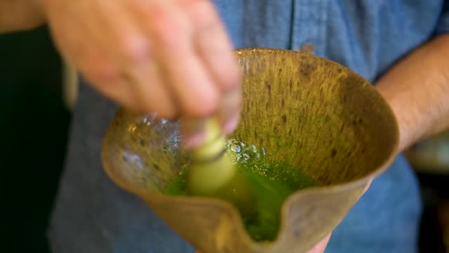 Closeup of hands mixing matcha in wooden cup in slow motion